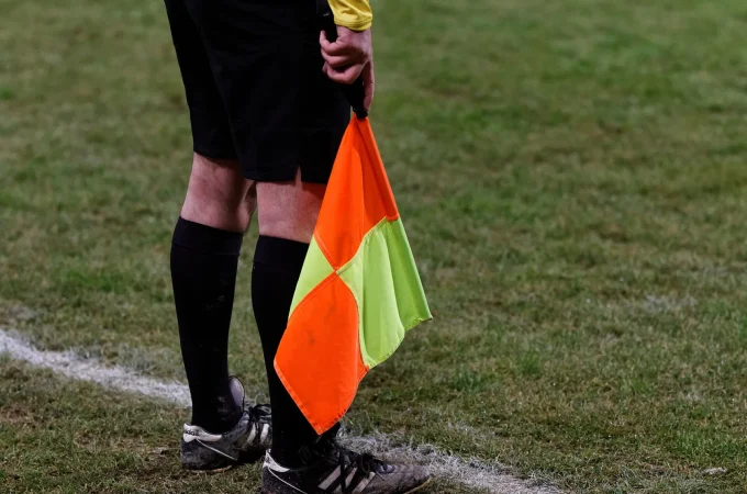 An assistant referee holding a flag beside a football pitch