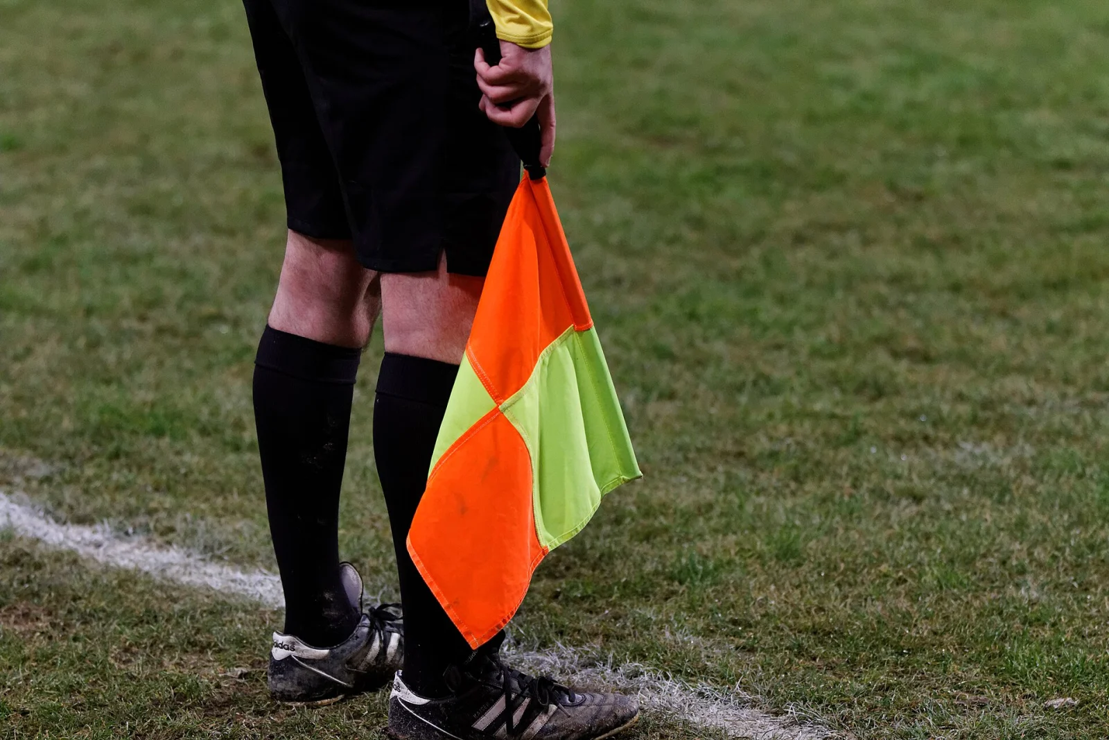 An assistant referee holding a flag beside a football pitch
